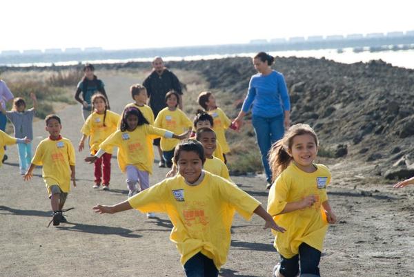 Children in yellow shirts running near a beach.